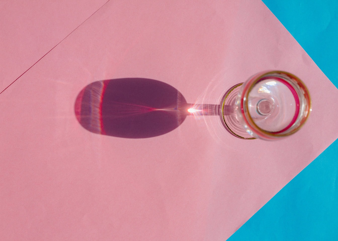 Un verre de cristal brillant avec son ombre sur une surface de papier rose