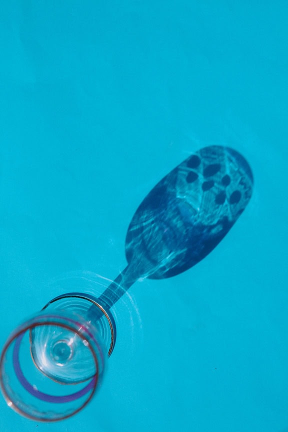 Un vaso de cristal con una sombra sobre una superficie azul