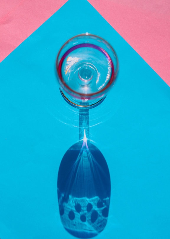 Copo de vinho de cristal com sombra em uma superfície azul e rosa pastel