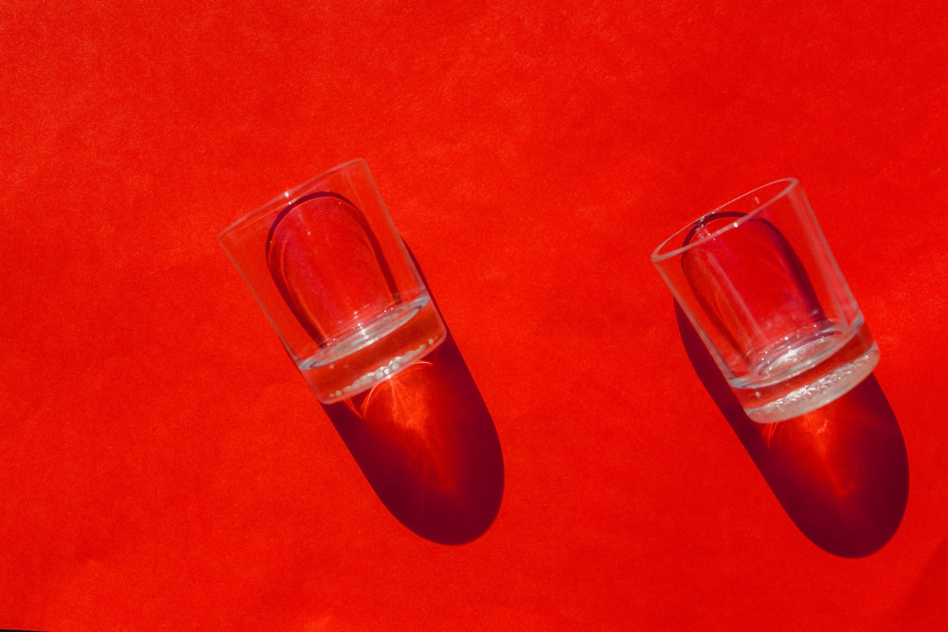 Transparent empty small glasses with shadows on a red surface