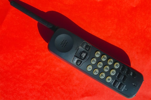 Um velho telefone sem fio preto de plástico com mostradores de silicone em uma superfície vermelha