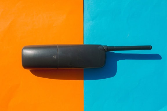 Old black wireless phone on a blue and orange background