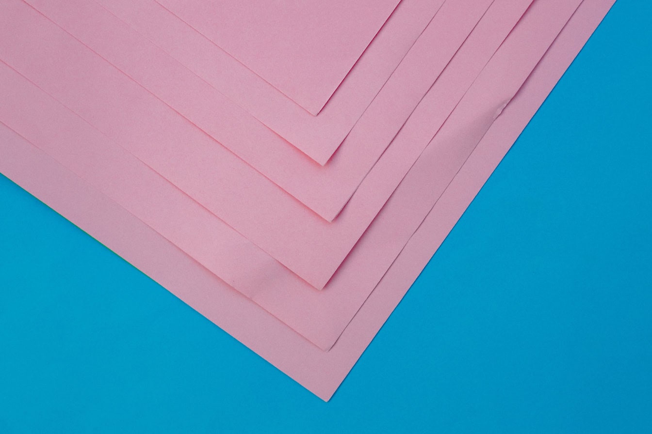 Pila de papel rectangular rosa sobre superficie azul, una textura de esquinas de papeles rosados