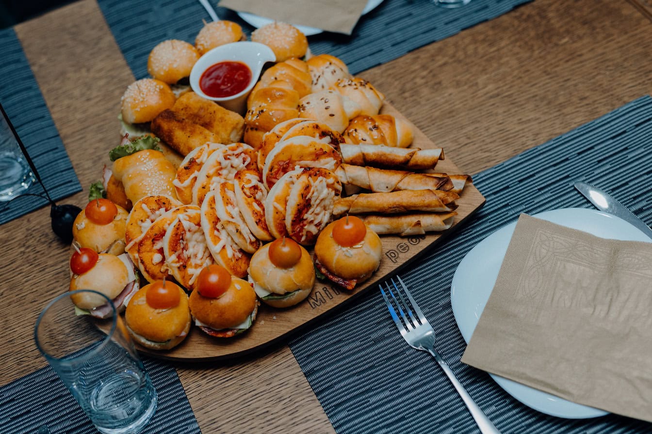 Ein herzförmiges Tablett mit Vorspeisen auf einem Tisch, verschiedene Sandwiches, Mini-Burger und Brötchen mit Käse