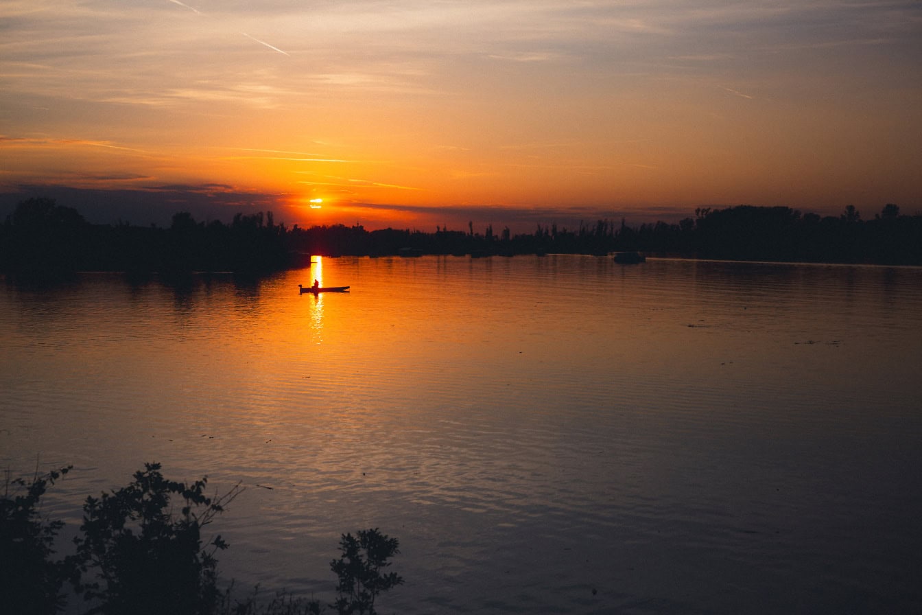 A silhouette of a small boat on a lake during sunset with orange-yellow sky