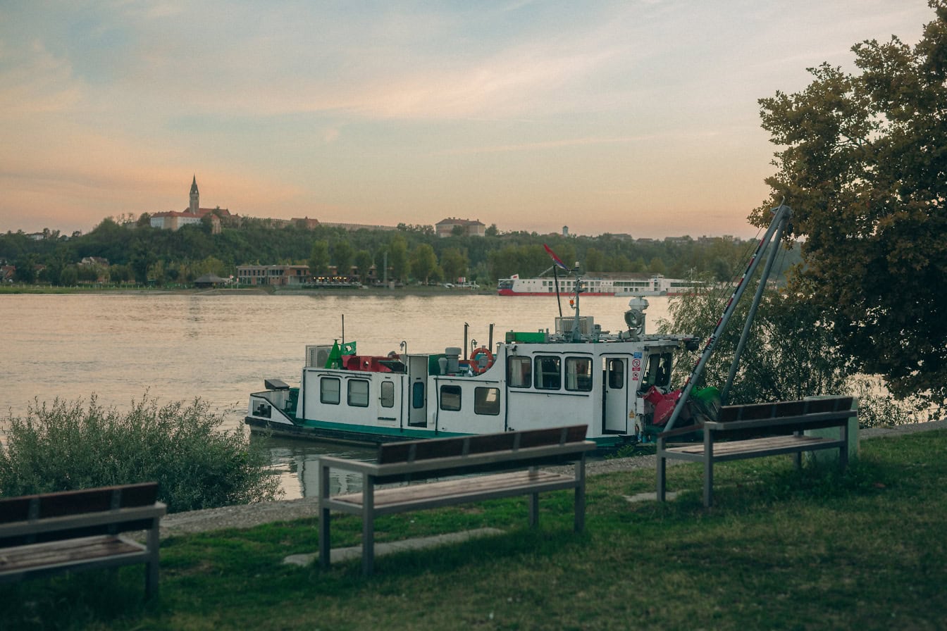 Sebuah perahu penggali di tepi sungai sungai Danube di Bačka Planka di Serbia dengan menara gereja di backgroun di Ilok, Kroasia