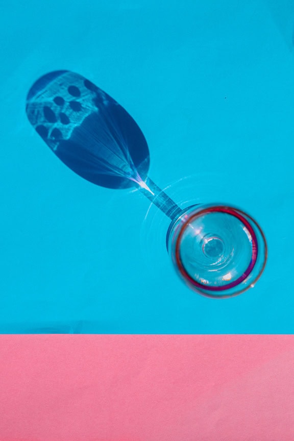 Vertical photo of a crystal wine glass with a shadow on the two-tone pink-turquoise blue background