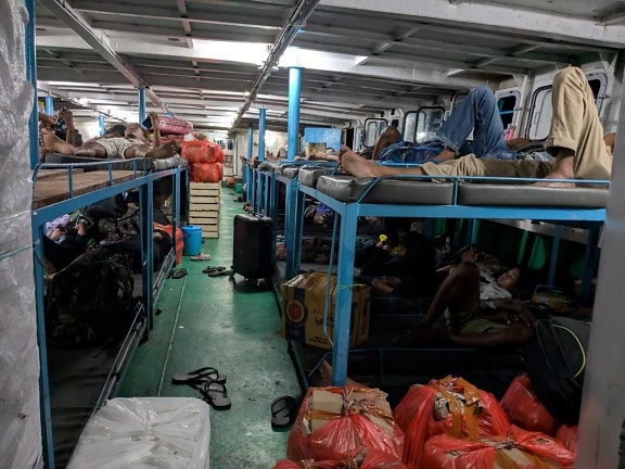 Overcovered deck of ship with people lying on bunk beds inside a ship