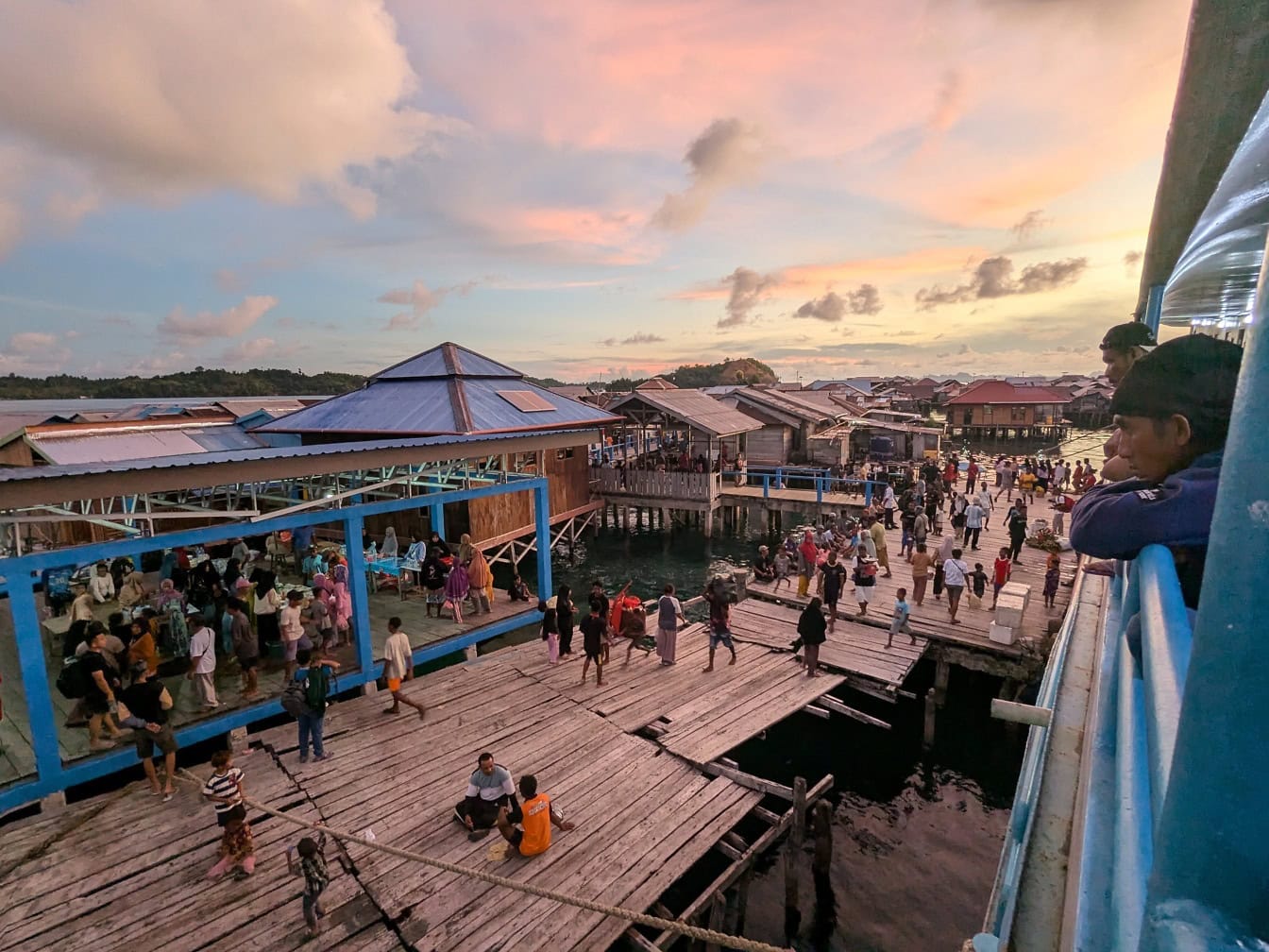 Una vista desde un barco turístico atracado en un muelle abarrotado con gente en un pueblo pobre con casas flotantes en el agua