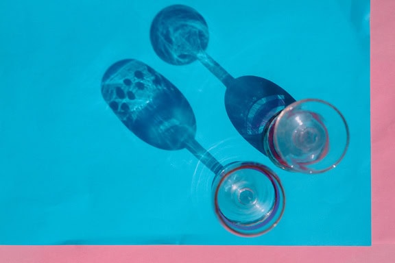 Two crystal wine glasses on a blue and pinkish surface