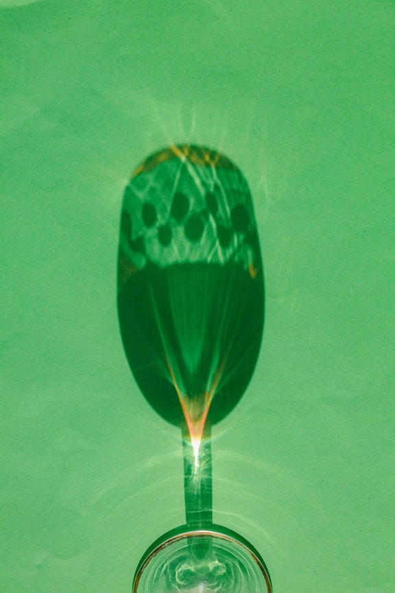 Long shadow of a crystal glass on a green background