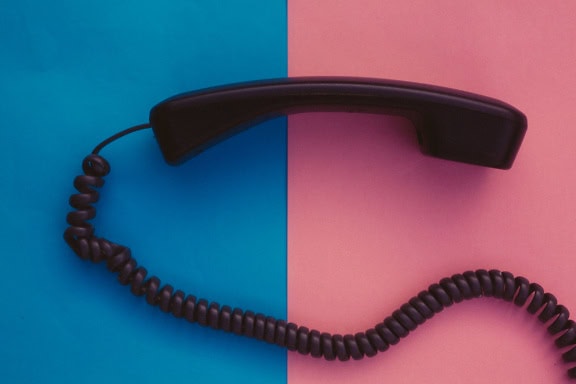 A handset of a telephone receiver with telephone cable on a two-tone blue and pink background