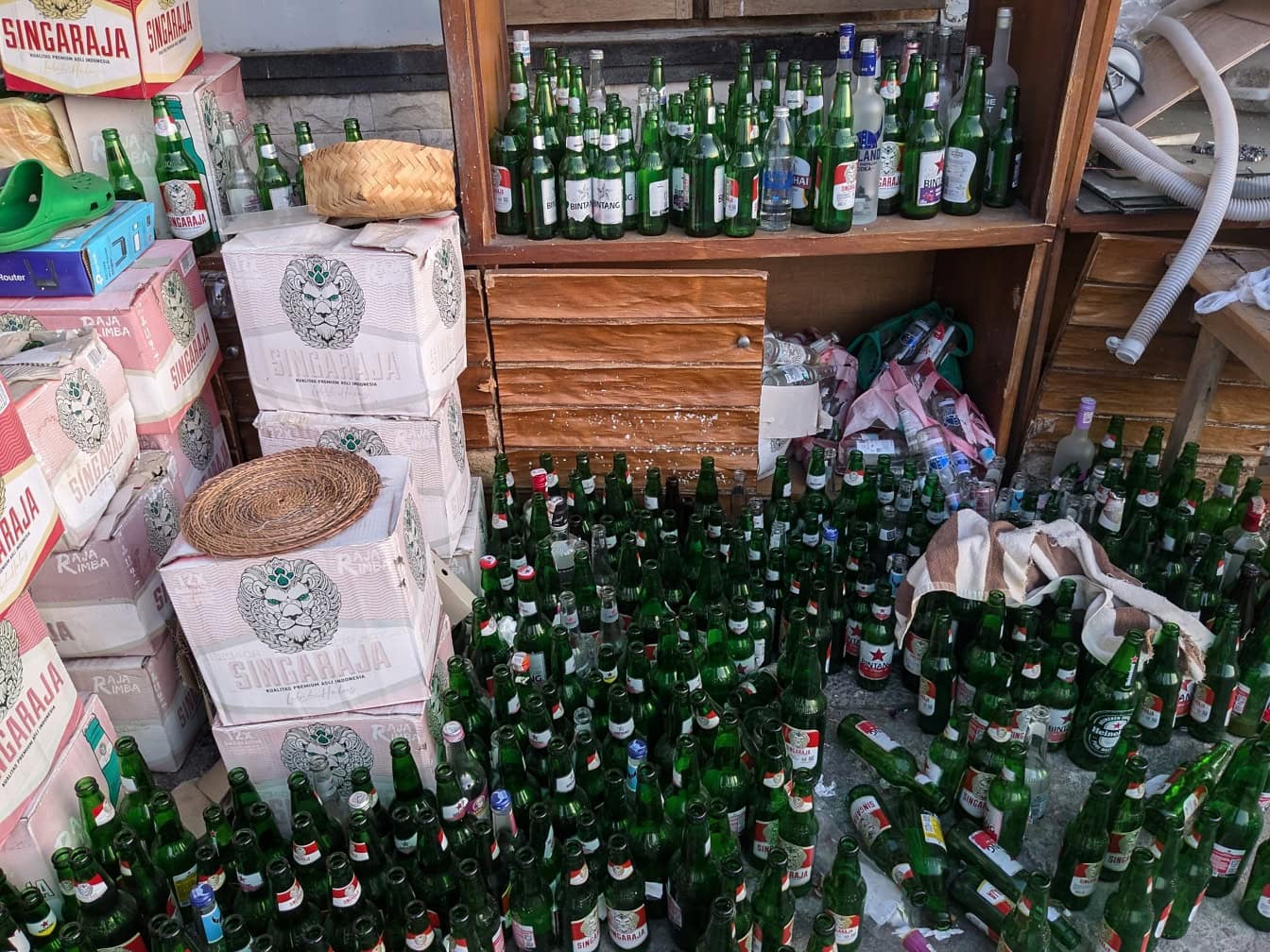 Un almacén de una tienda con muchas botellas vacías en el suelo junto a cajas de cerveza