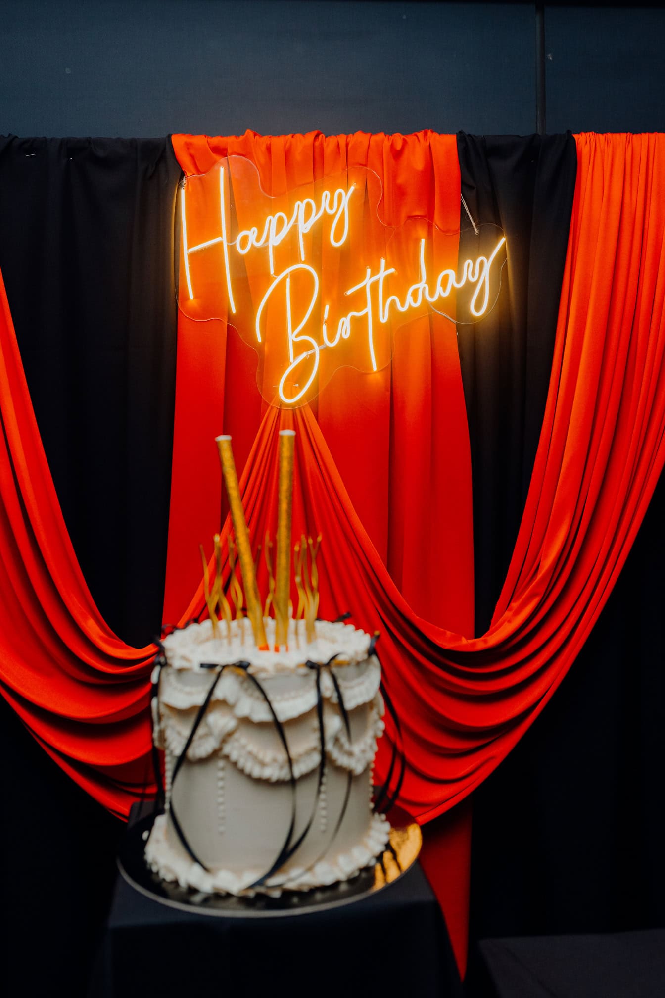 Insegna al neon illuminata Happy Birthday su tenda glamour rosso scuro e nero e torta di compleanno con candele