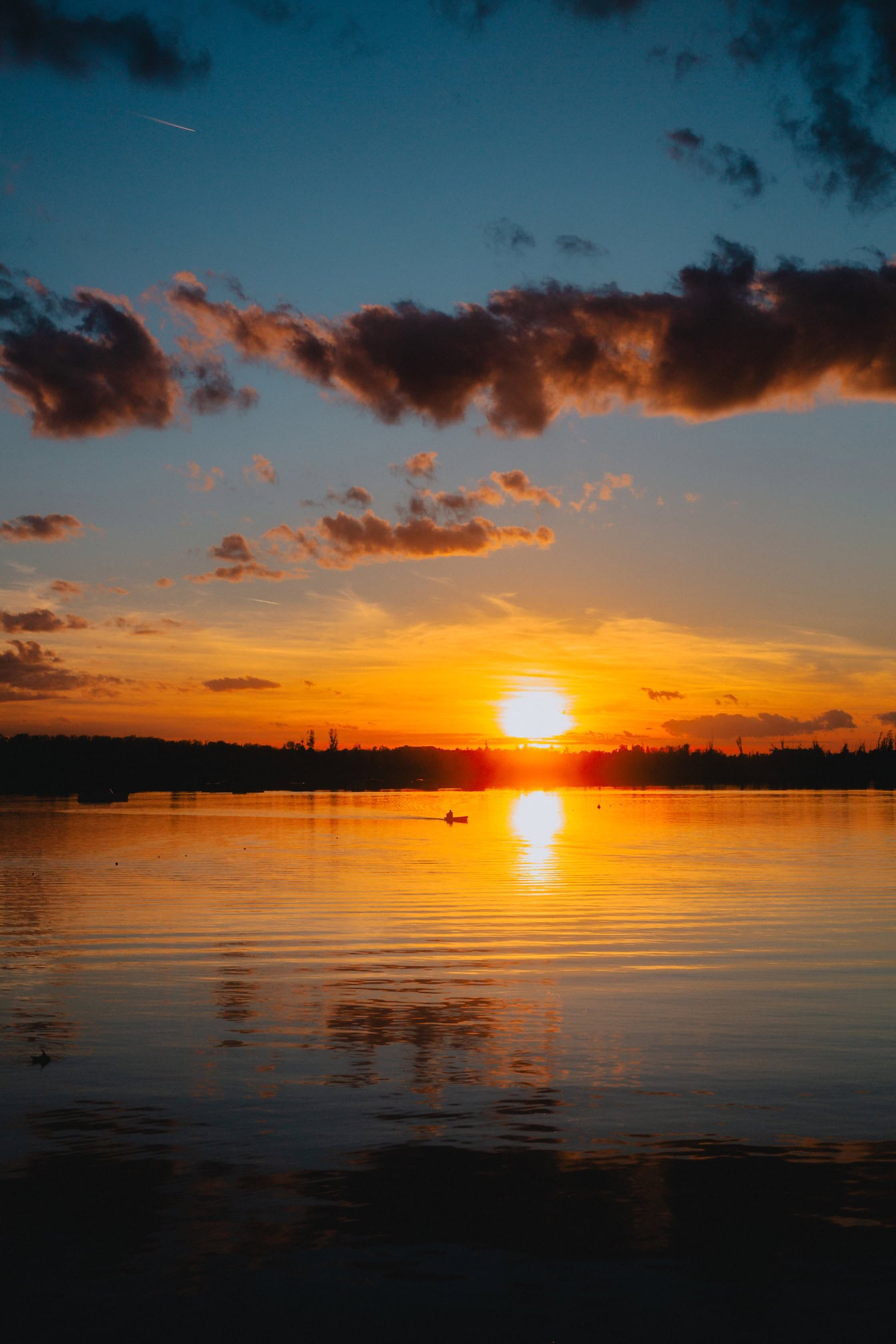 Vibrant vertical photograph of sunset over water with dark clouds at sky