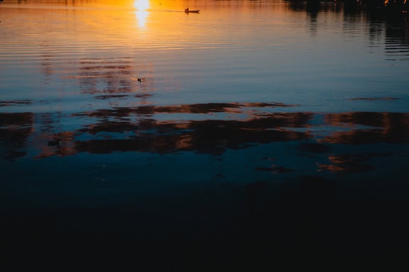 Paesaggio di tarda serata al lago con tramonto scuro e riflessione del sole sull’acqua