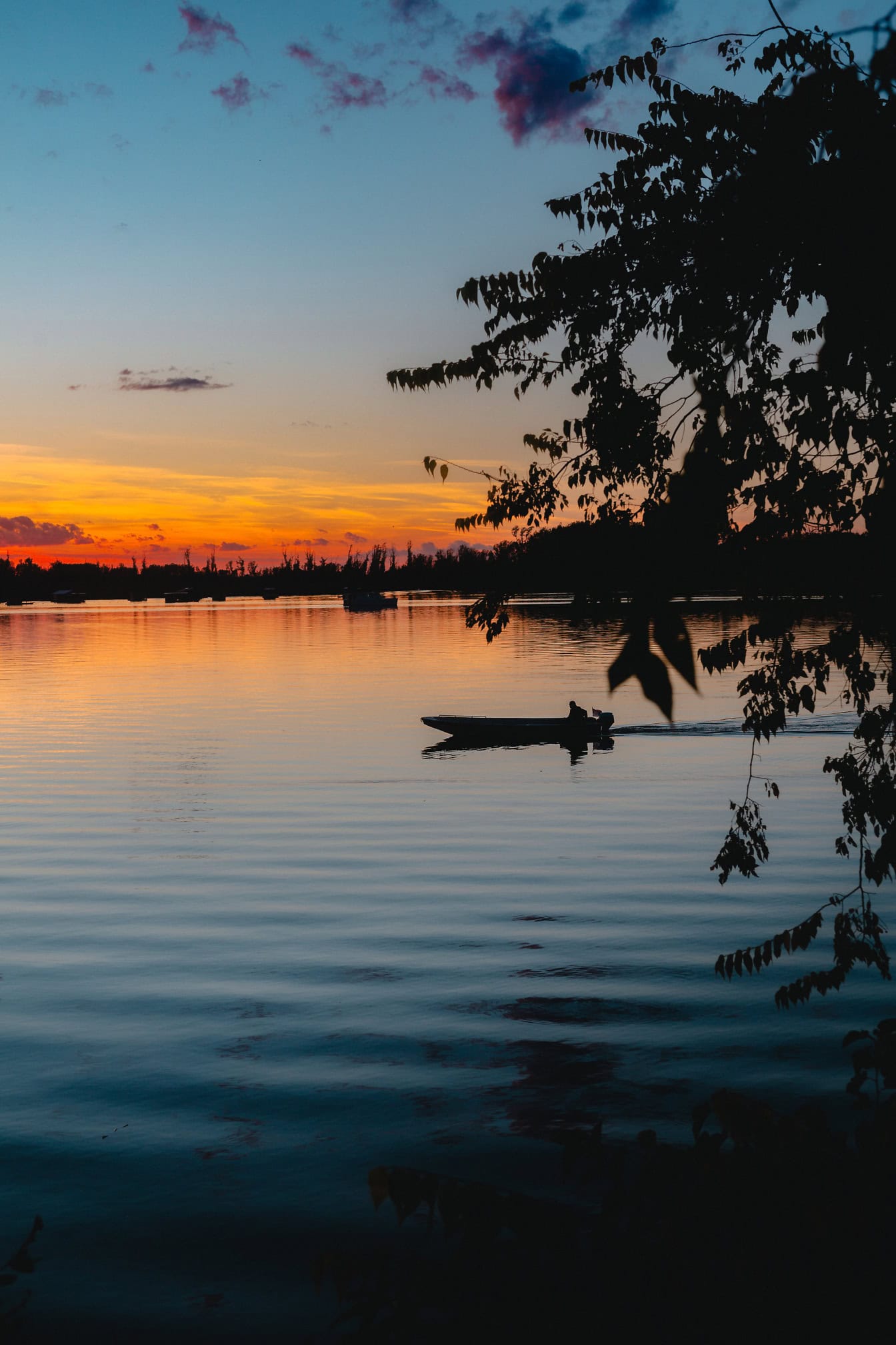 Silhouette eines kleinen Fischerboots auf dem Wasser, das bei Sonnenaufgang vom Sonnenlicht beleuchtet wird