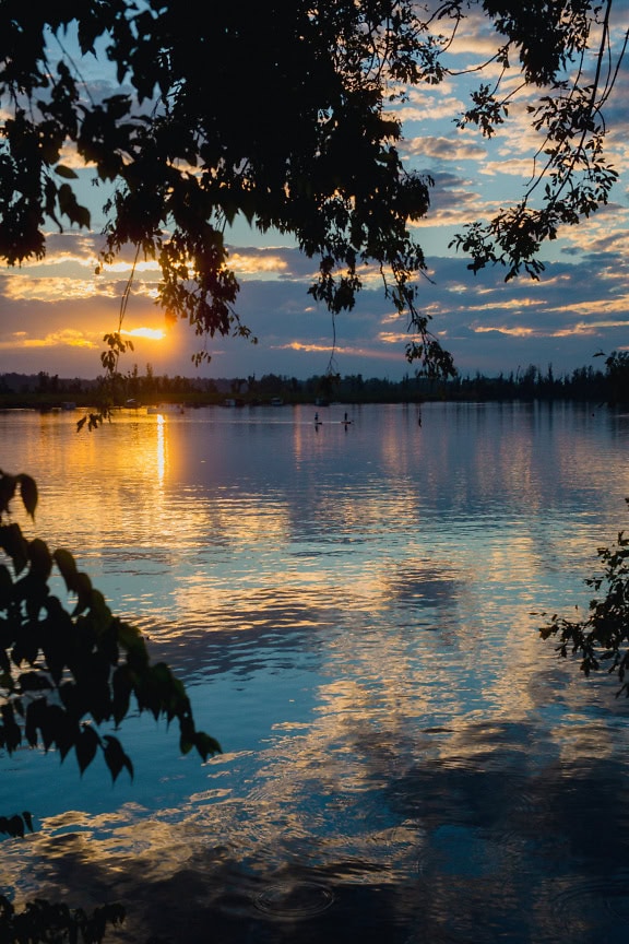 Apus de soare peste un lac cu reflexia cerului înnorat pe orizontul de apă calmă