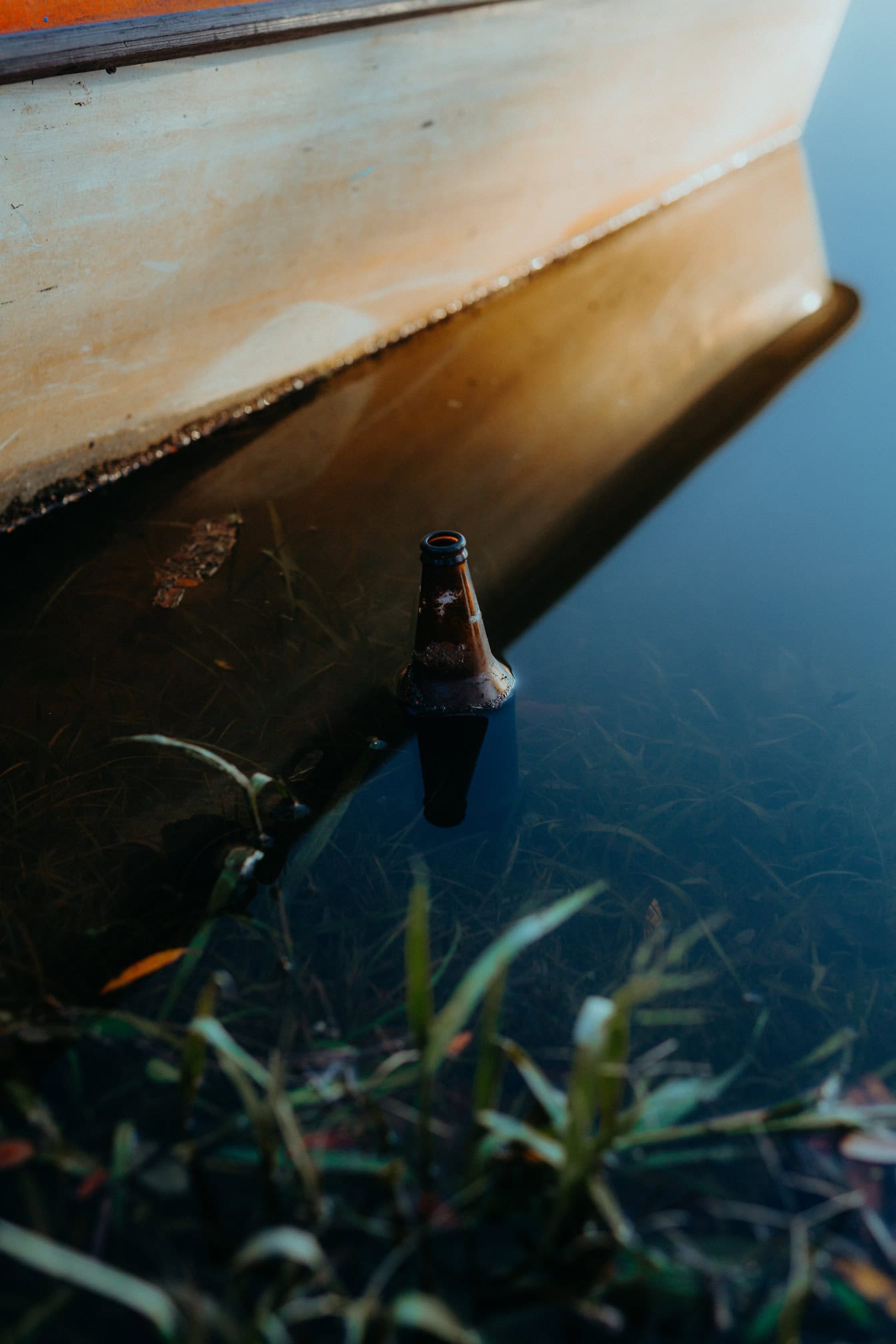 Botella marrón en el agua junto a un barco, una contaminación de las vías fluviales por los residuos de vidrio