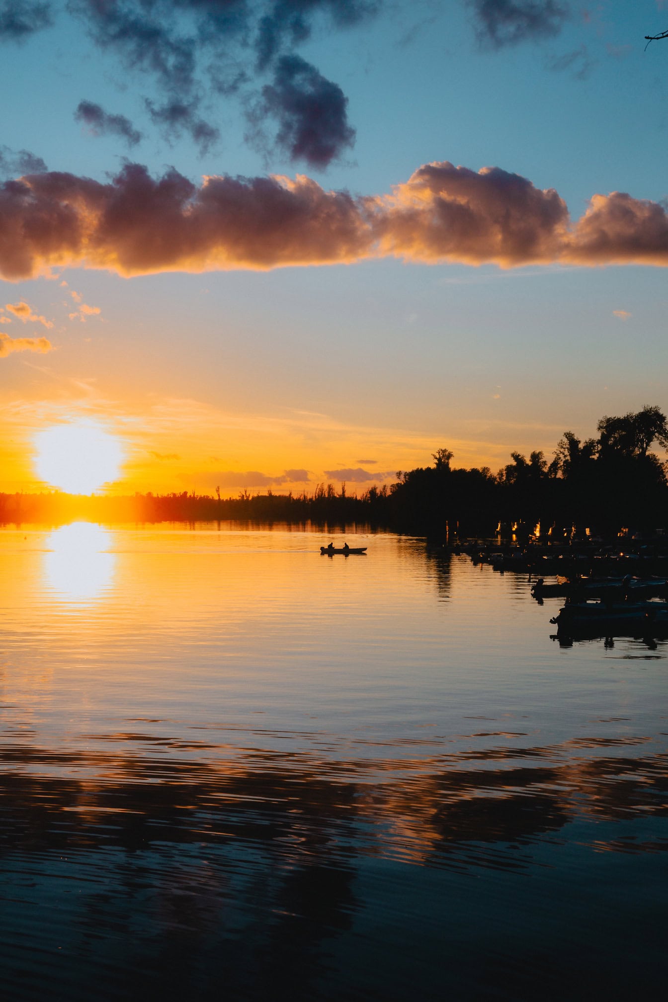 Dramatisk solnedgang med levende sollys over en sø med silhuet af både i havnen