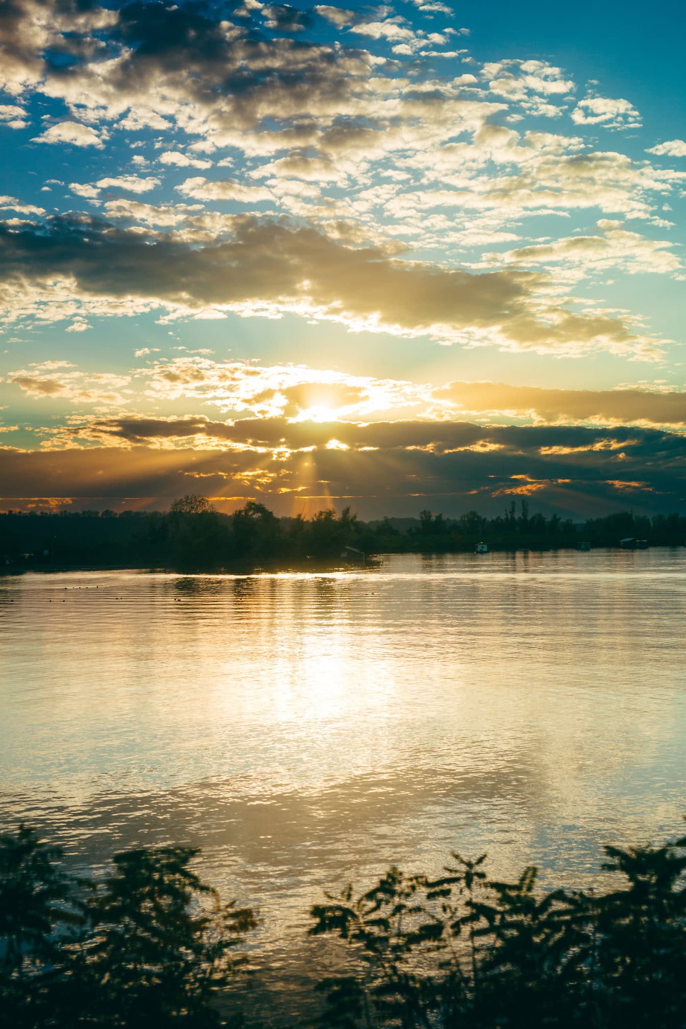 Soarele strălucește printre nori deasupra unui lac