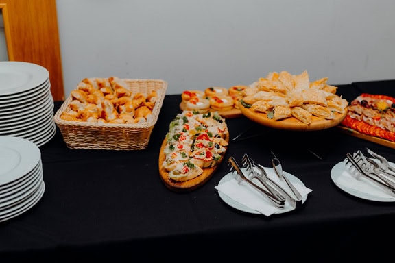 Table with small sandwiches, pies, donuts and rolls next to ceramic plates