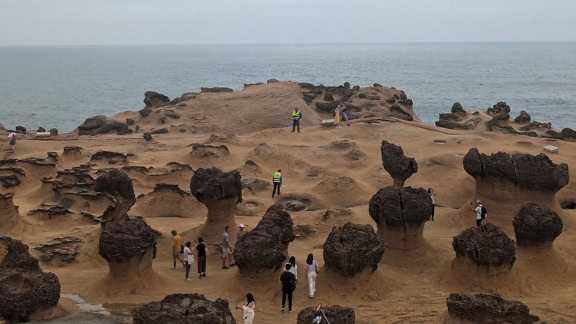 Sekelompok wisatawan berdiri di daerah berpasir di tepi laut dengan formasi batuan aneh di geopark Yehliu, tanjung di distrik Wanli, New Taipei, Taiwan