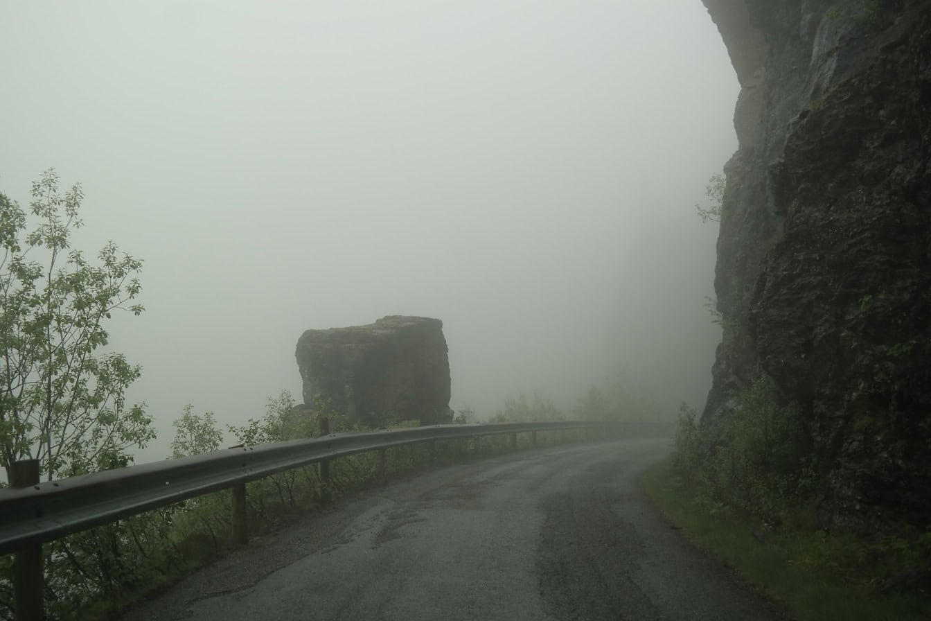 Ein dichter Nebel über einer Asphaltstraße mit Sicherheitszaun, ein nebliger Tag im norwegischen Hochland