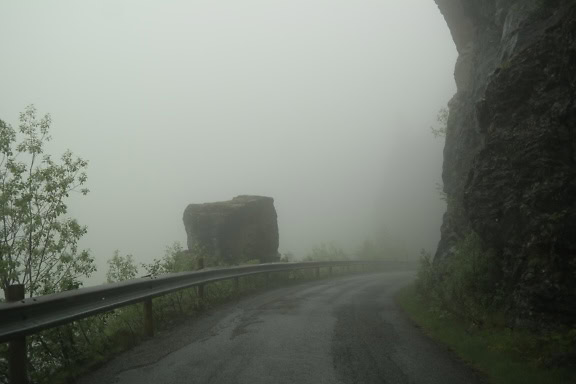 Ein dichter Nebel über einer Asphaltstraße mit Sicherheitszaun, ein nebliger Tag im norwegischen Hochland