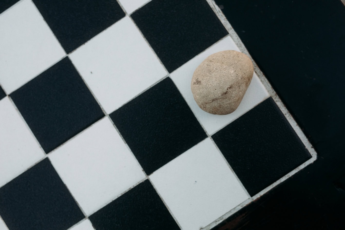 A pebble on a chessboard, a close-up of a stone on a black and white square checkered background