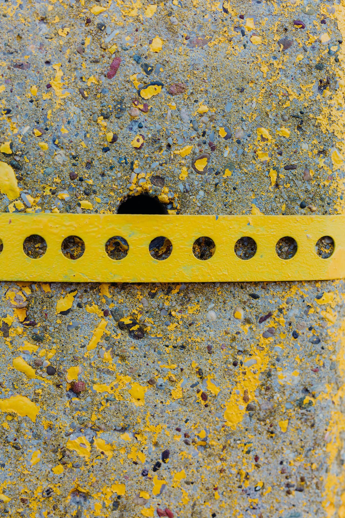 A yellow metal strip with holes on concrete painted with yellowish paint that is peeling, and