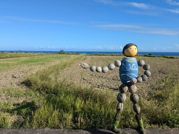 A scarecrow made out of wood in a countryside field by road