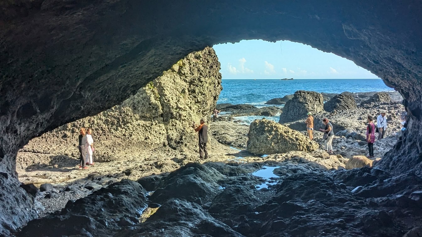 People standing on a rocky beach in front of geological wonder, a natural sea cave at Shimen Banshaojiao recreation area near Hualien, Taiwan