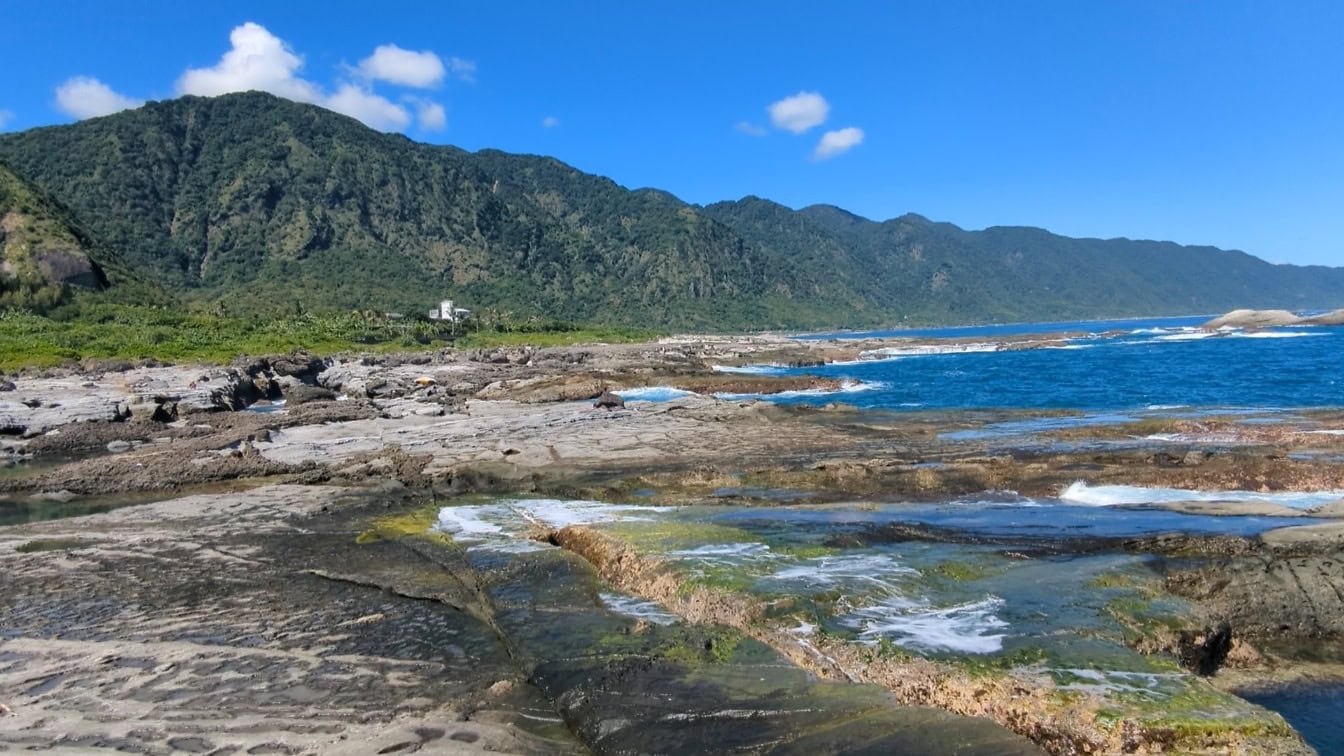 Scenă de coastă în Taiwan cu plajă stâncoasă cu apă și munți în fundal