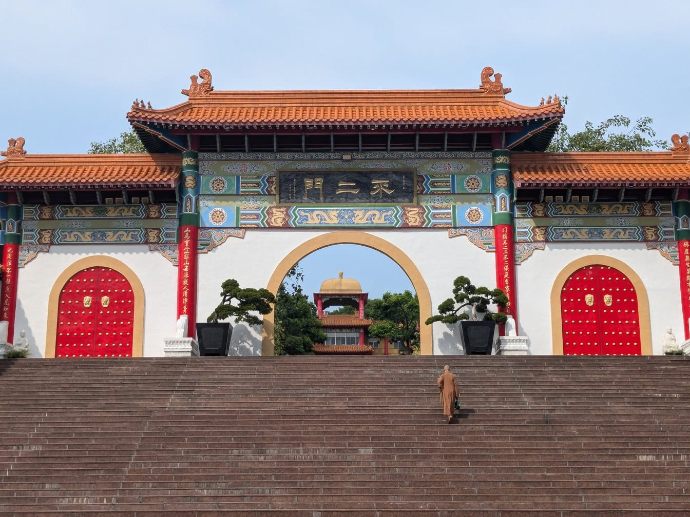 Pintu masuk dengan gerbang utama biara Fo Guang Shan dengan seorang biksu Buddha berjalan menaiki tangga, Taiwan, Asia