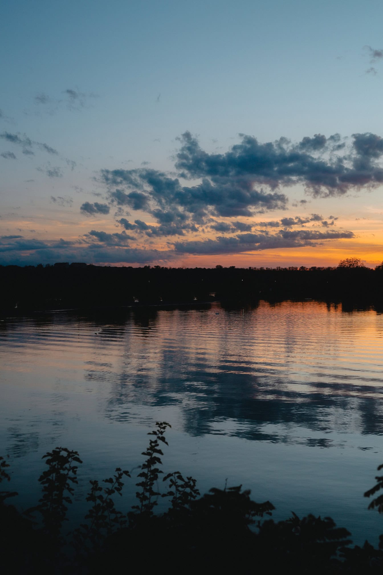 A landscape photograph of a lakeside just before sunrise with water and silhouette of trees