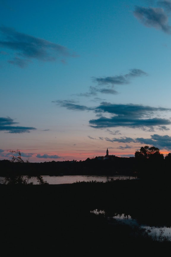 Verticale landschapsfotografie ‘s nachts van een water met een silhouet van toren in de verte