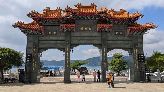 Tourists standing under a large archway in traditional Chinese architectural style, part of Wen Wu Temple at the Sun Moon Lake in Yuchi Township, Nantou County, Taiwan