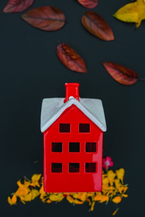 Ceramic figurine of red house with white roof and dark leaves around it on a black background