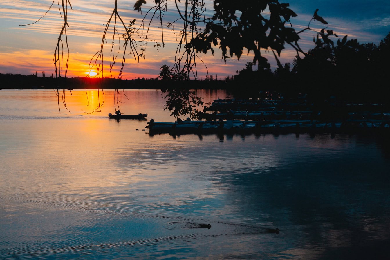 Auringonlasku järven sataman yllä pienten moottoriveneiden silueteilla