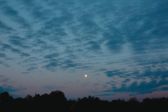 Moon in the cloudy dark blue sky at twilight