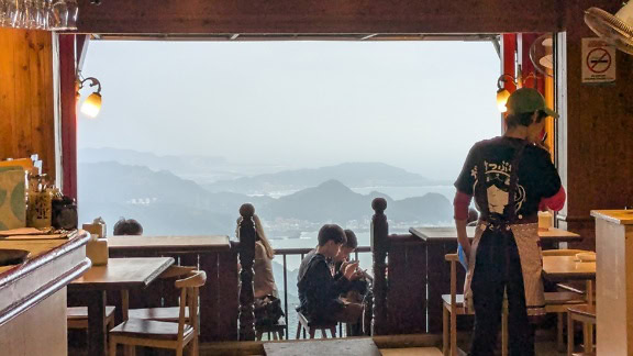 Folk sidder ved borde på en restaurant i Taiwan med udsigt til bjerge og vand