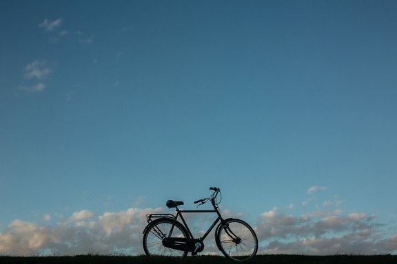 Side view of a black bicycle on a hilltop under blue sky with clouds