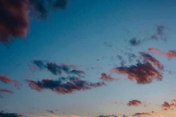 Blauer Himmel mit dunklen Wolken, die das Sonnenlicht in der Abenddämmerung kurz nach Sonnenuntergang in einem niedrigen Winkel reflektieren