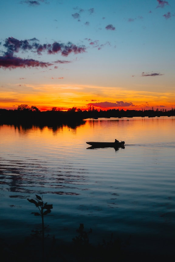 夕暮れ時の夕暮れ時の水面に小さなモーターボートのシルエットがある湖畔の垂直風景写真