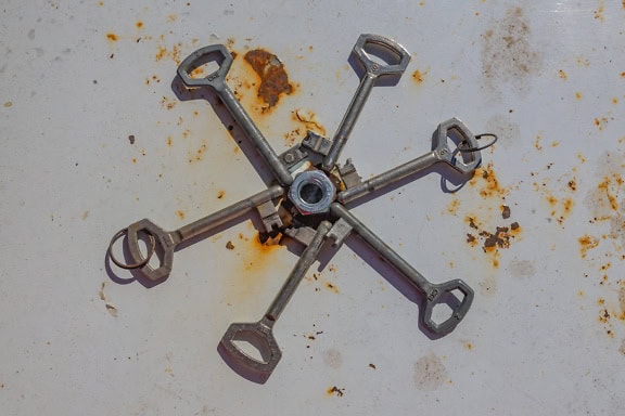 A warded lock keys around stainless steel nut on rusty metal surface painted white