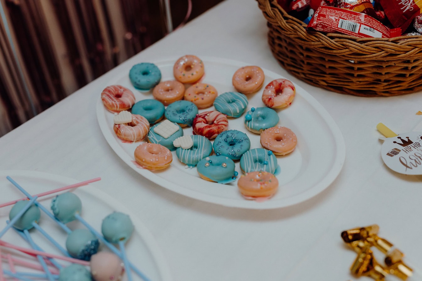 Plato de donas en miniatura en plato, piruletas y otros deliciosos dulces en una mesa puesta para una fiesta de cumpleaños