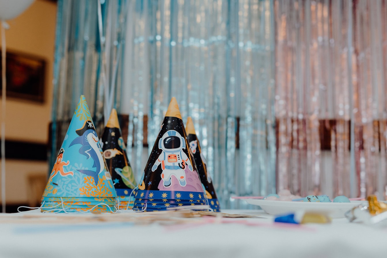 Chapeaux en papier de fête d’anniversaire avec des illustrations amusantes sur eux sur une table dressée pour l’anniversaire d’un enfant