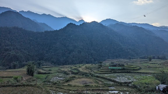 The sunlight coming out from behind the hilltops, the landscape of the valley with the mountains at sunrise