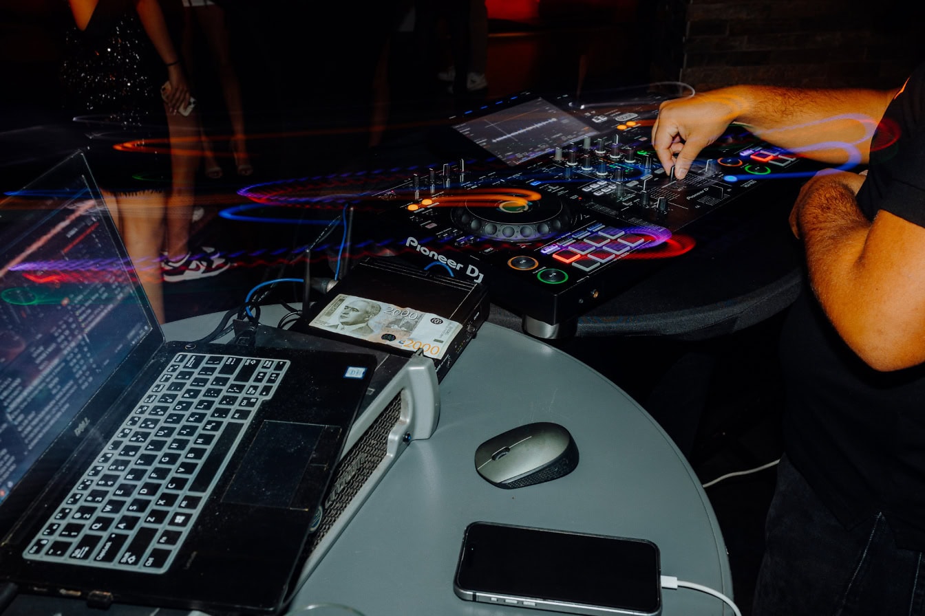 Een diskjockey of een DJ die een geluidsmixer en een laptop gebruikt om populaire muziek te spelen op een feest in een nachtclub